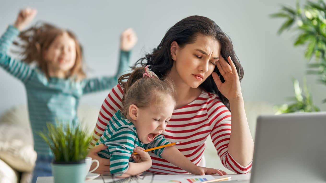 mother surrounded by children while trying to work looking stressed