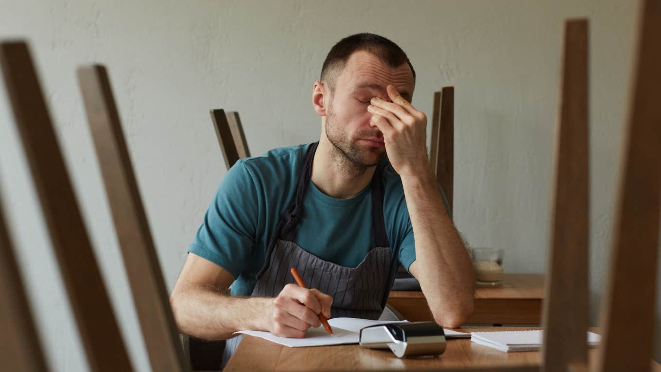 exhausted young man calculating finances and doing inventory at small business shop