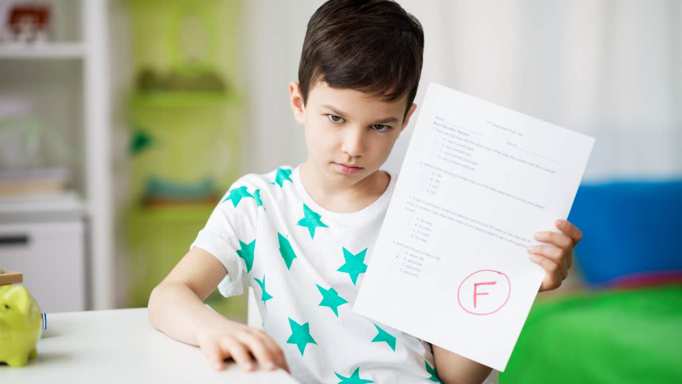 little boy holding a school assignment with an F grade