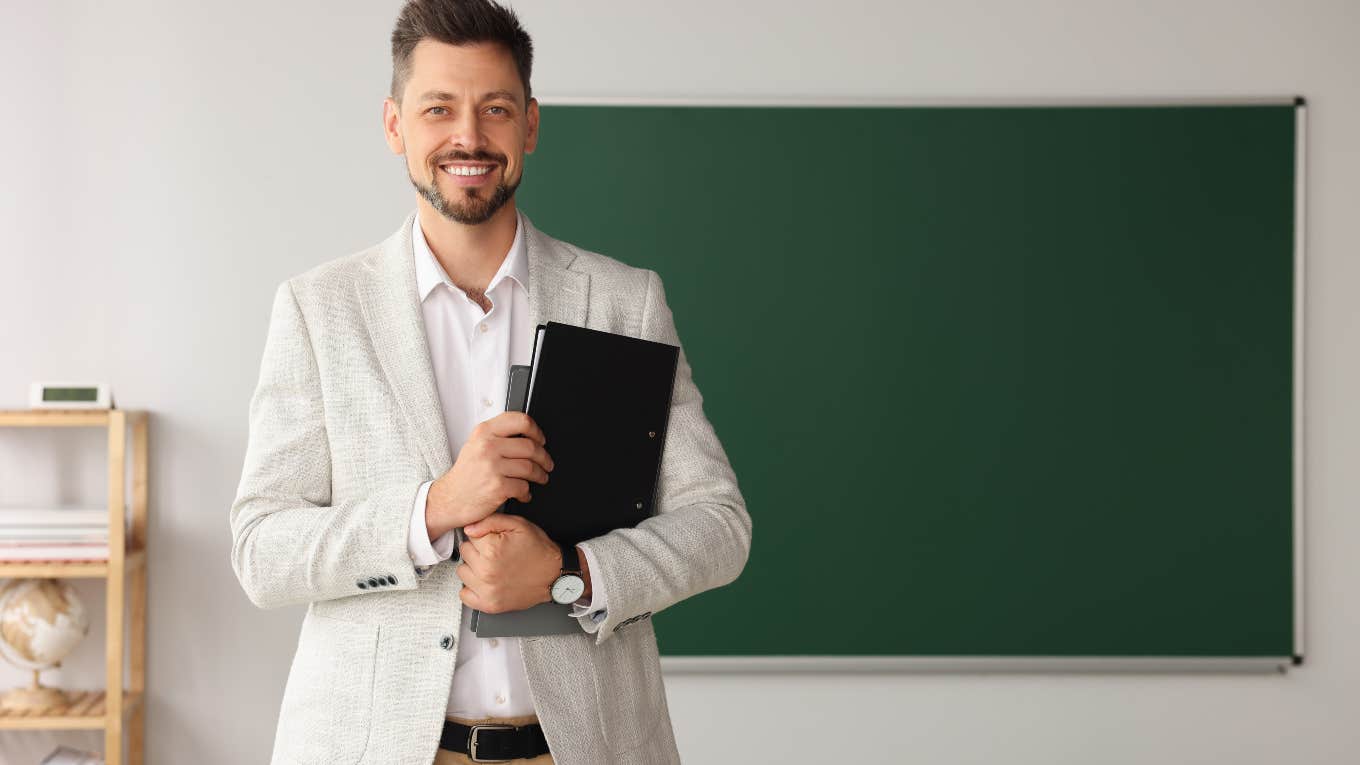 male teacher holding notebook standing in front of blackboard