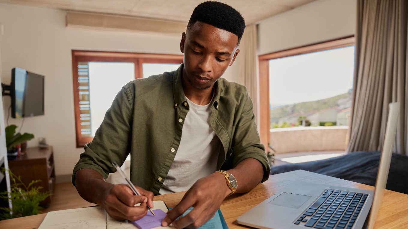 Man writing on sticky notes at his desk. 