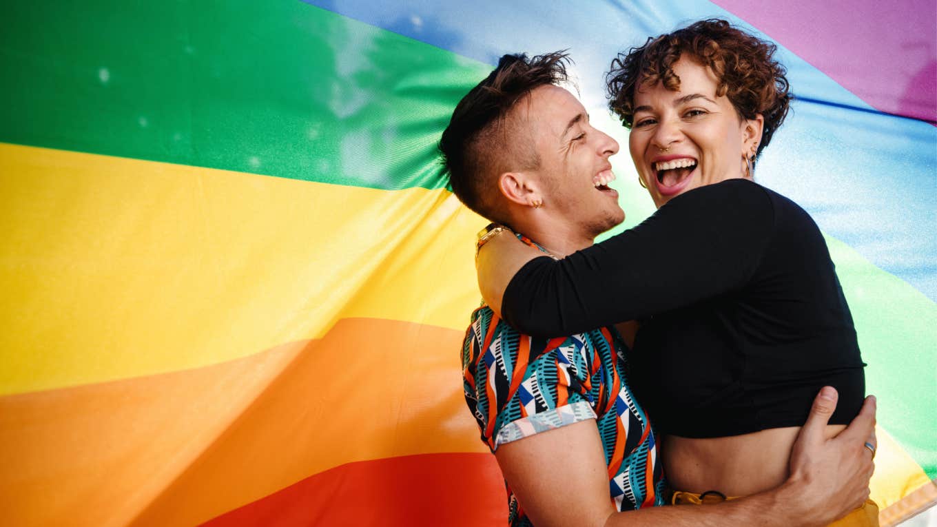 queer couple embrace each other in front of pride flag