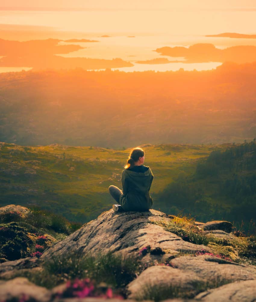 woman sits on rockface from elevated altitude admiring nature