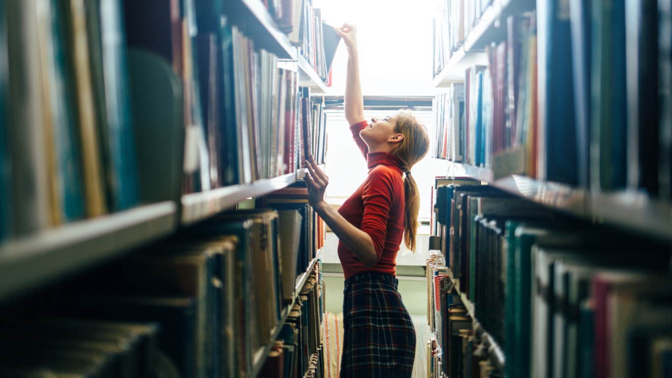 Woman taking book from library bookshelf.
