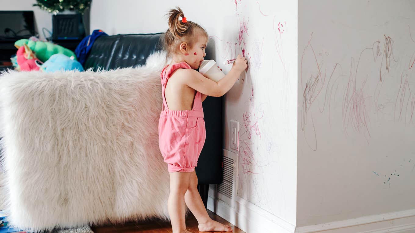 toddler girl drawing on the wall with a crayon