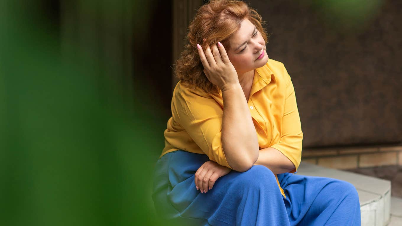 middle aged woman sitting on sidewalk thinking about something