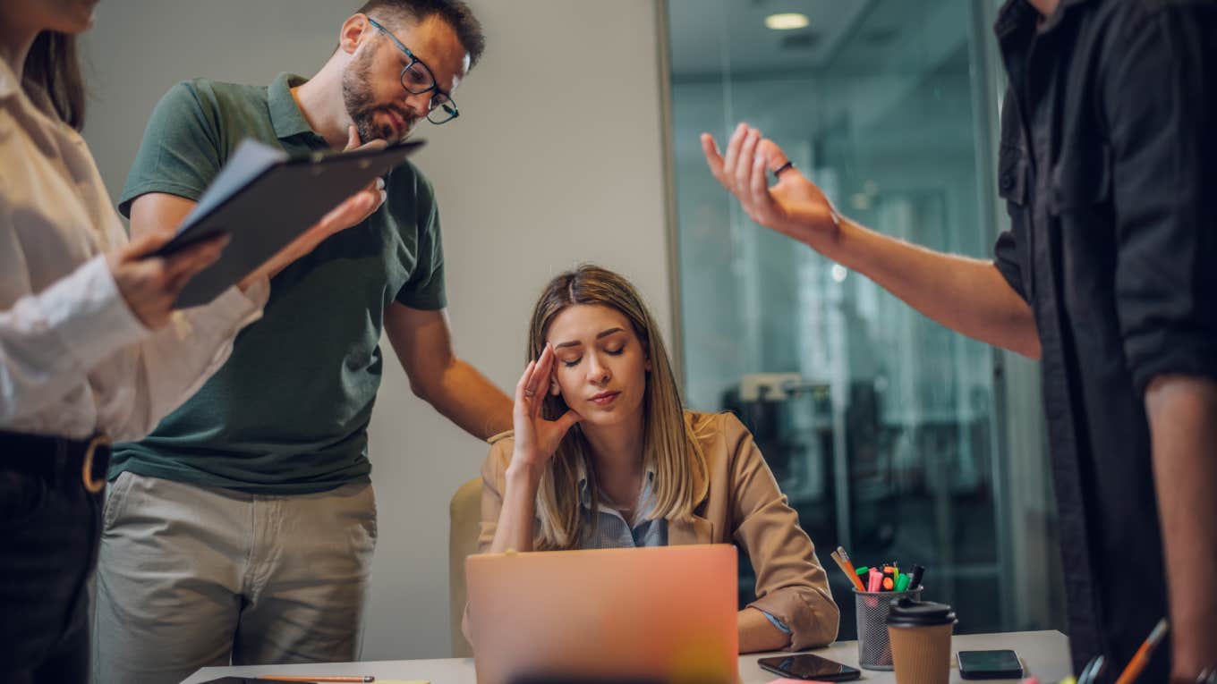 stressed employee sitting at desk in front of laptop with colleagues