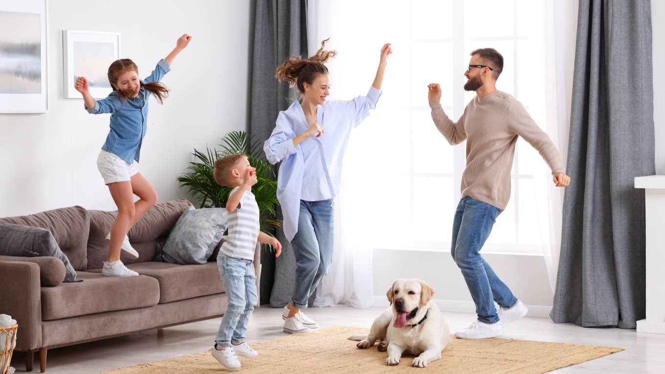 family of four jumping and dancing in living room with dog