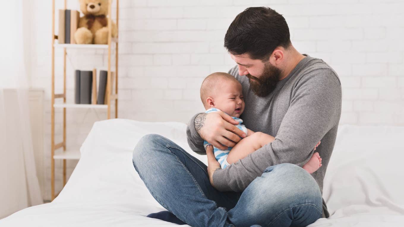 dad trying to calm crying baby down on bed at home