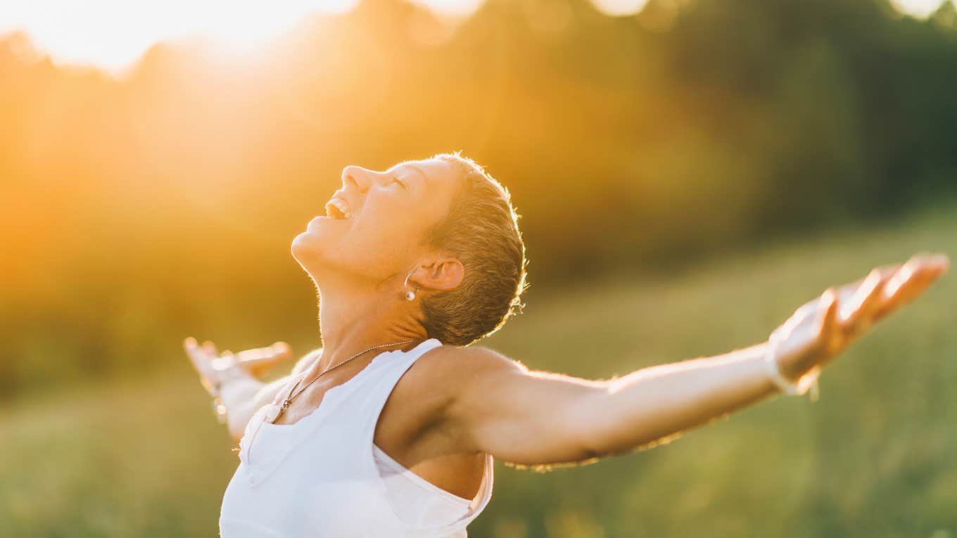 spiritual woman outside during sunset opens arms wide to receive positive energy 