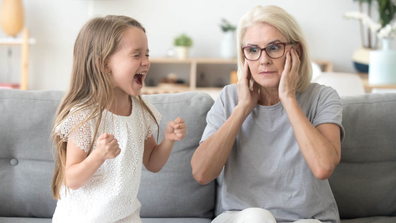 grandma holding down ears and feeling overwhelmed babysitting misbehaving grandkid 