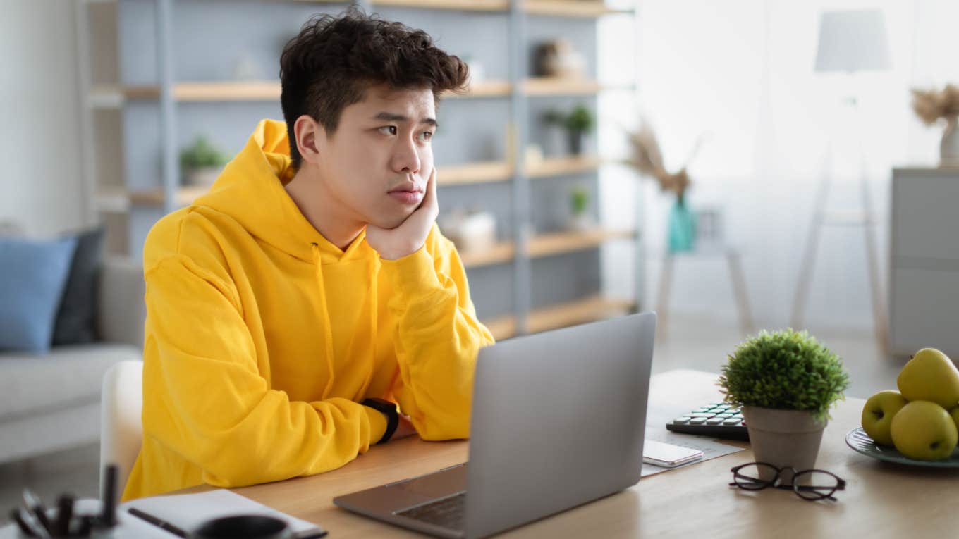 bored teenager sits at desk in front of laptop wondering what to do