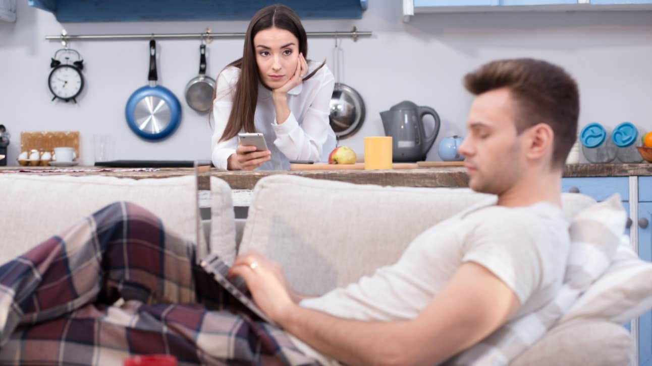 working wife resents work-from-home husband typing on computer on couch