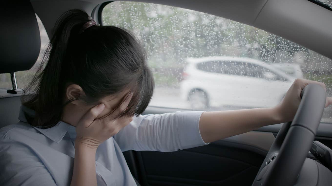 sad woman cries into hands in car while raining outside