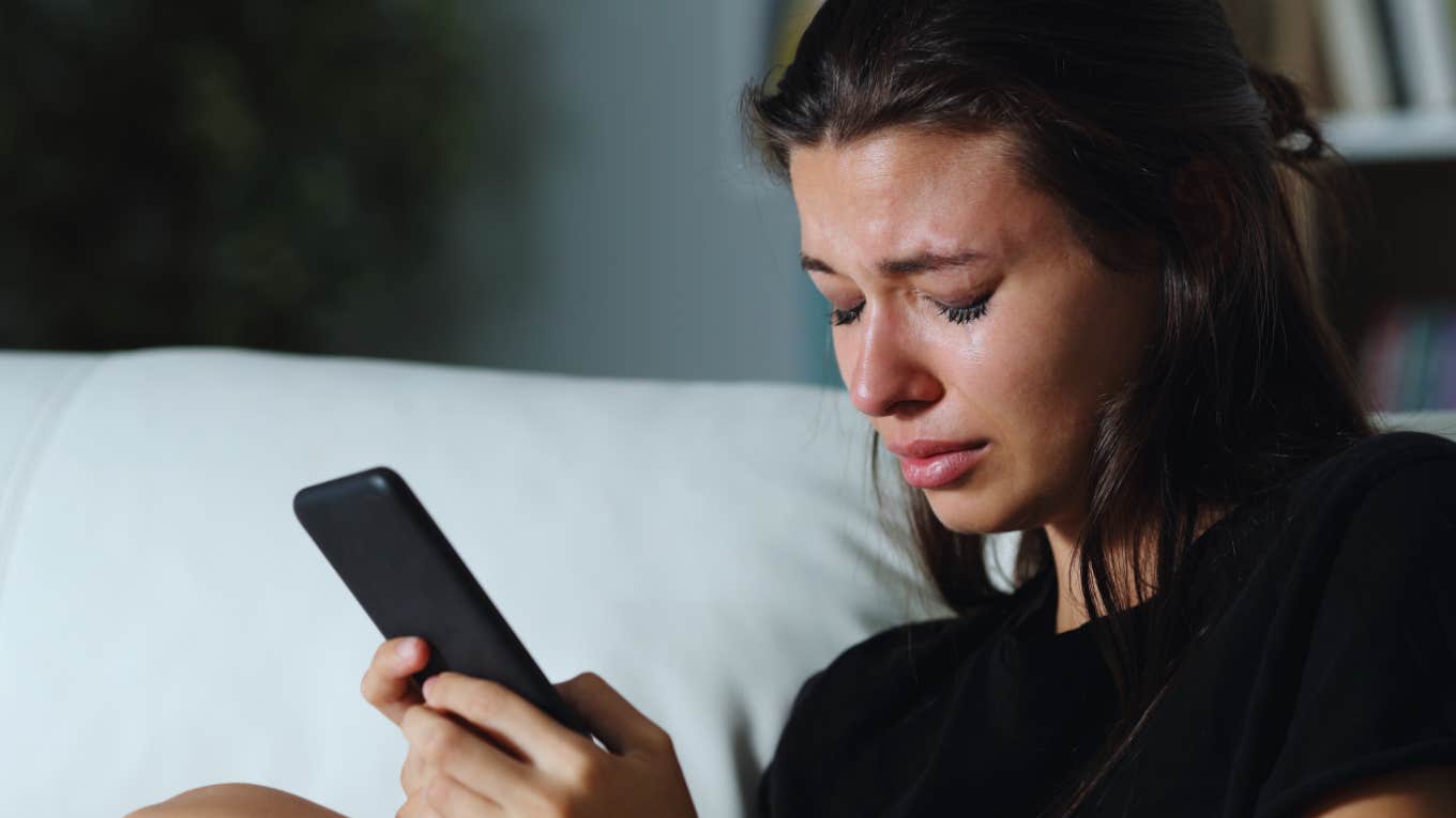 woman cries on couch while waiting for response on phone