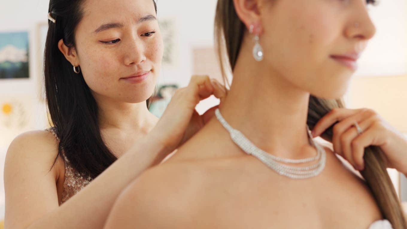 woman puts on necklace for bride on wedding day