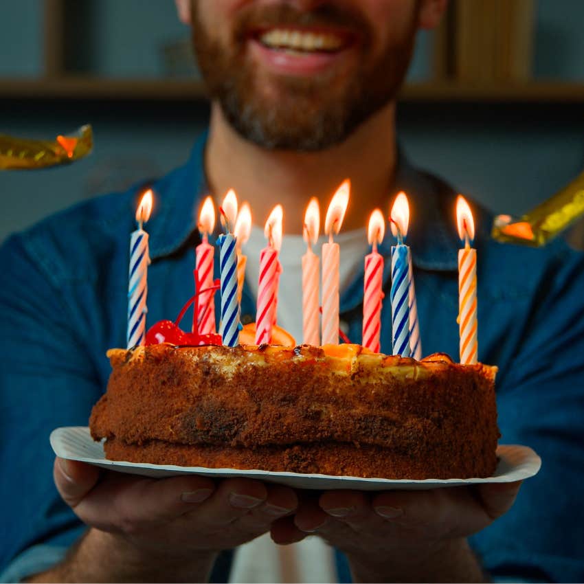 Man holds cake with birthday candles lit. 