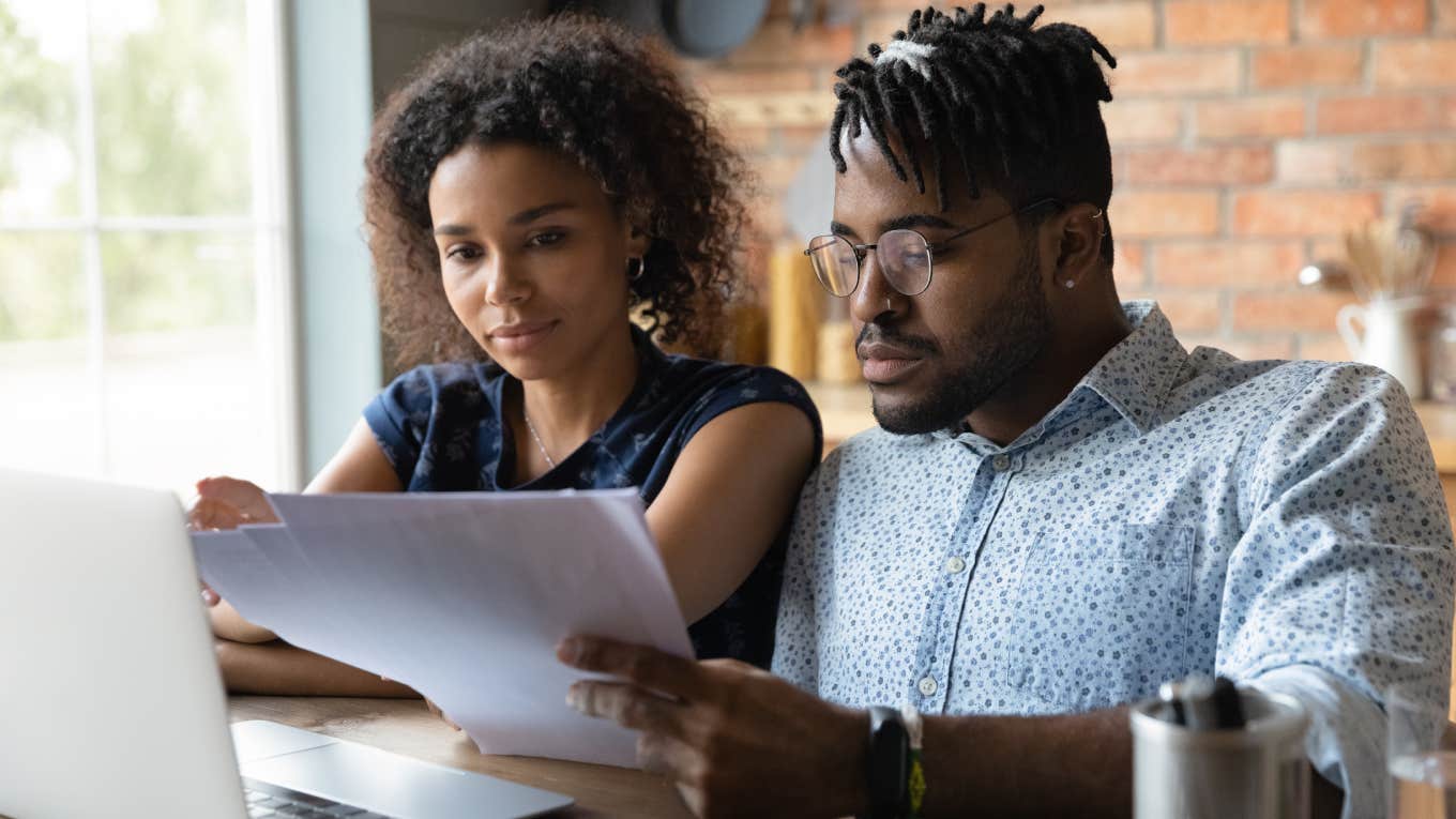 black couple sitting at desk looking at papers in front of laptop