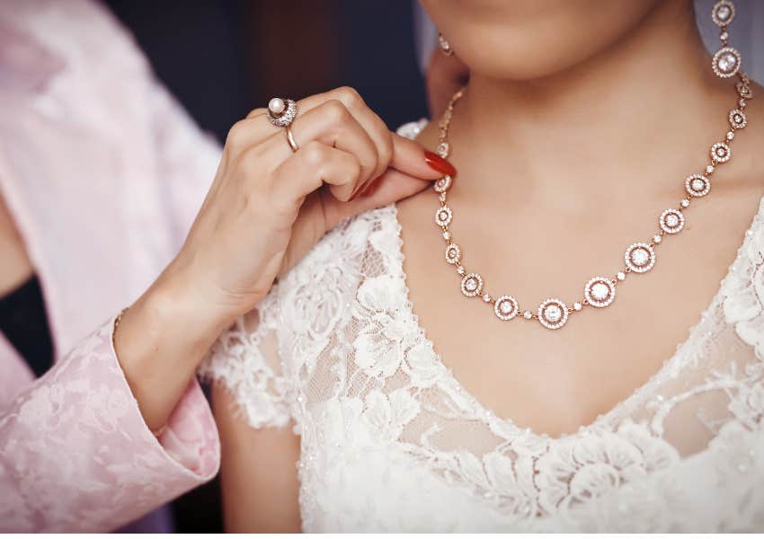 woman puts necklace on for bride on wedding day