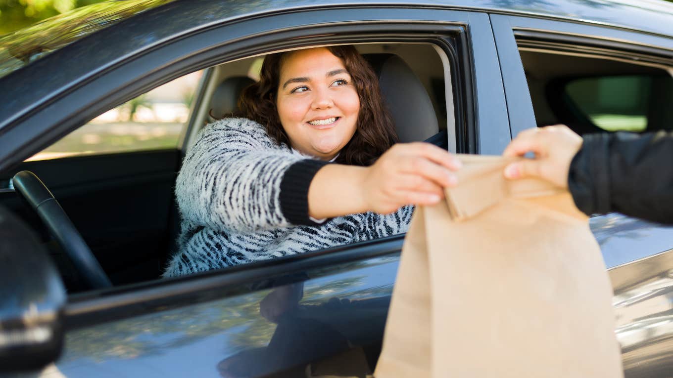 Woman in the Burger King drive thru grabbing a bag of food. 