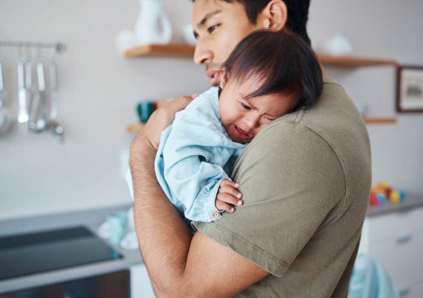 dad holding crying baby son in kitchen