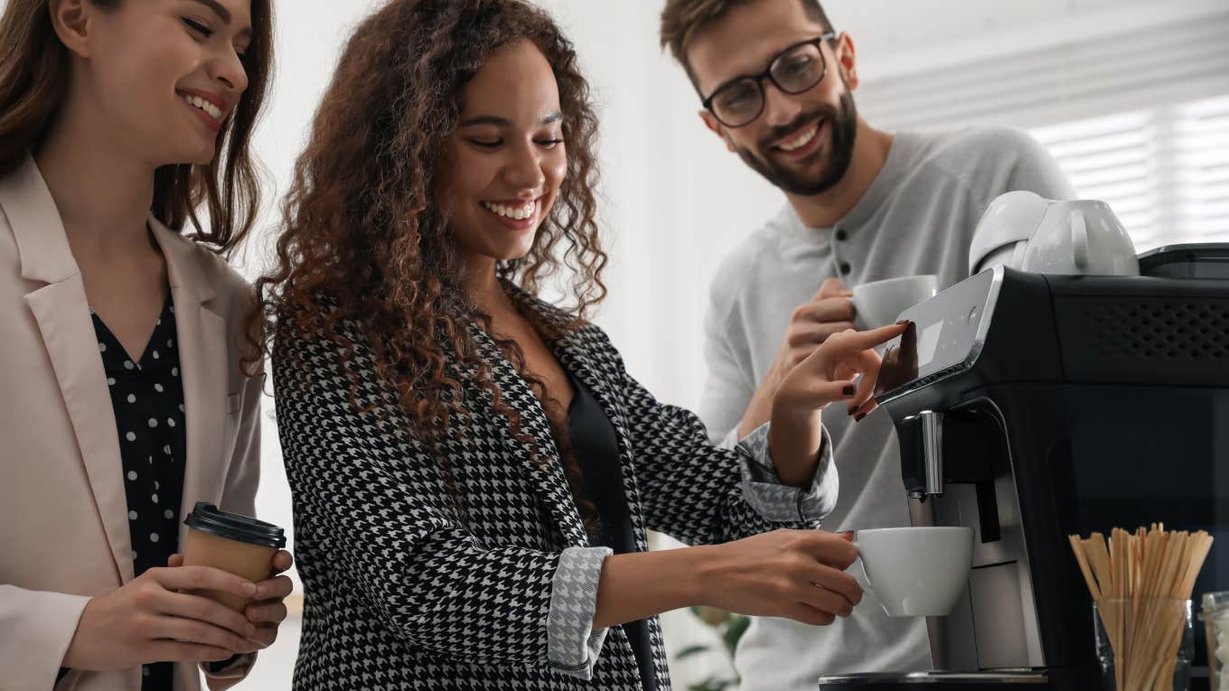 woman talking with colleagues while using modern coffee machine in office