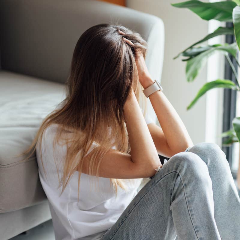 upset young woman sitting on floor with head in hands