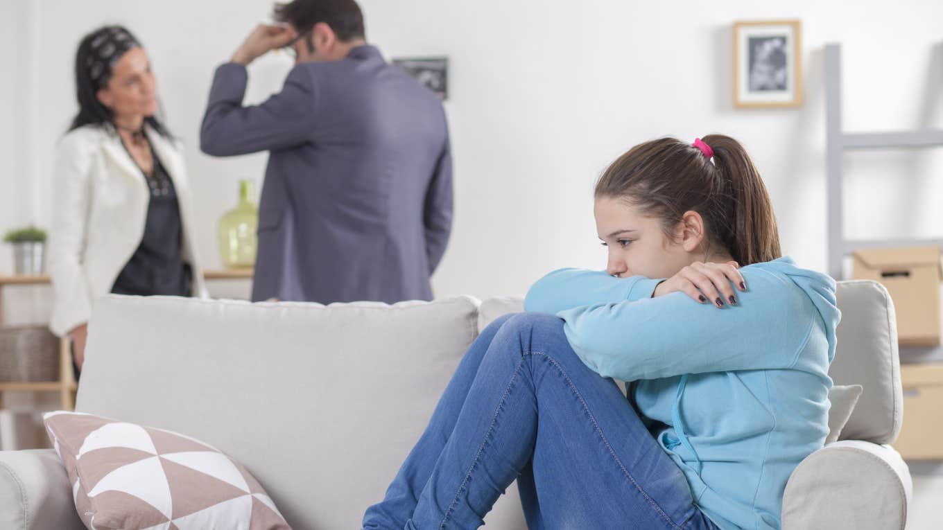 upset teenage girl sitting on couch while parents argue behind her