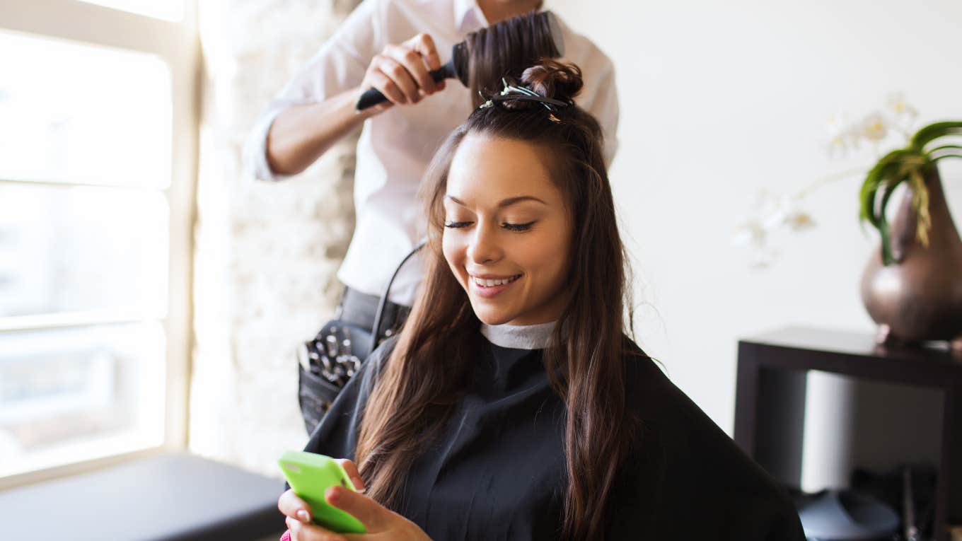 girl getting her hair done while looking at her phone