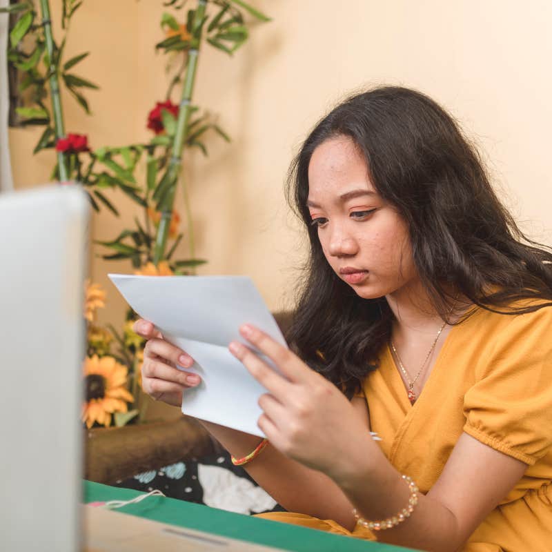 serious young woman sitting in front of laptop reading paper