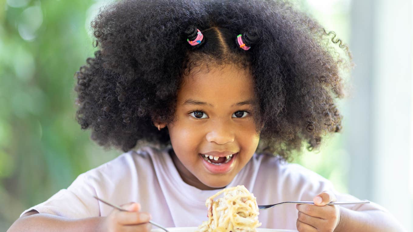 little girl smiling eating pasta