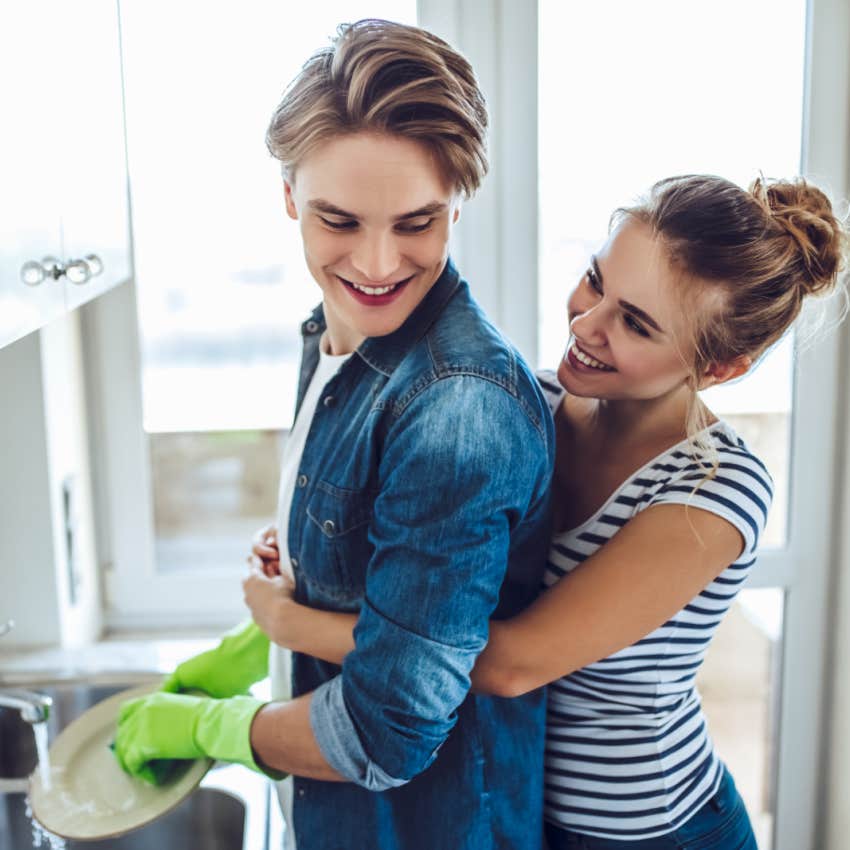 husband doing dishes while wife hugs him