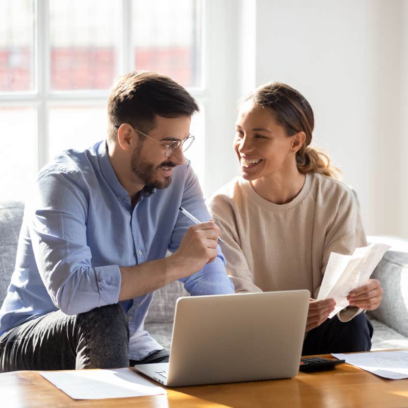  young married couple sit on couch calculating expenses