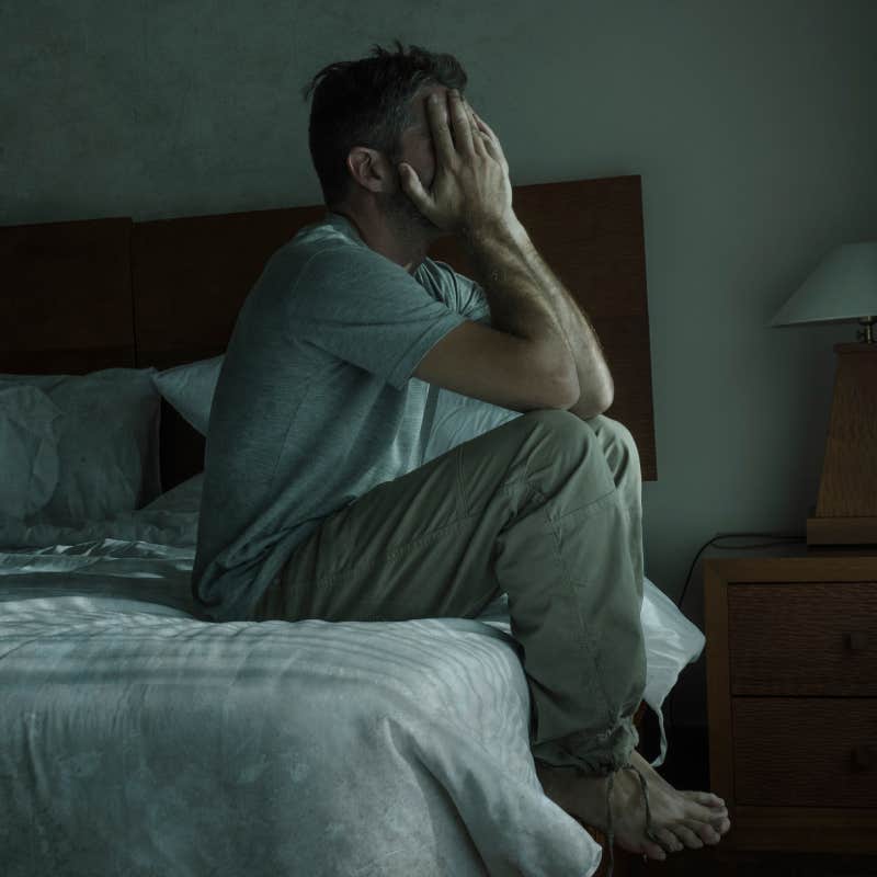 depressed and upset man sitting at the edge of bed with face in hands