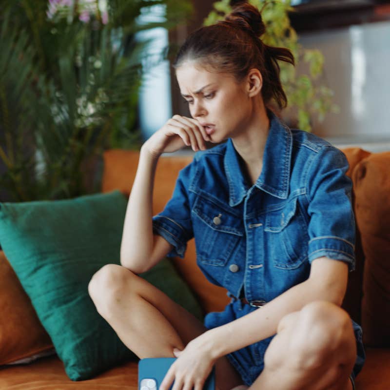 Stressed woman sitting on couch with hands on face and book in front of he