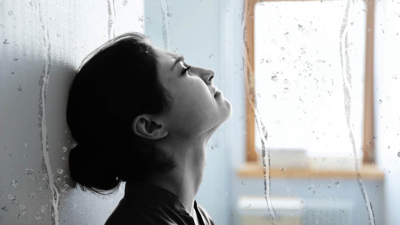 Woman grieving loss, leaning against wall crying 