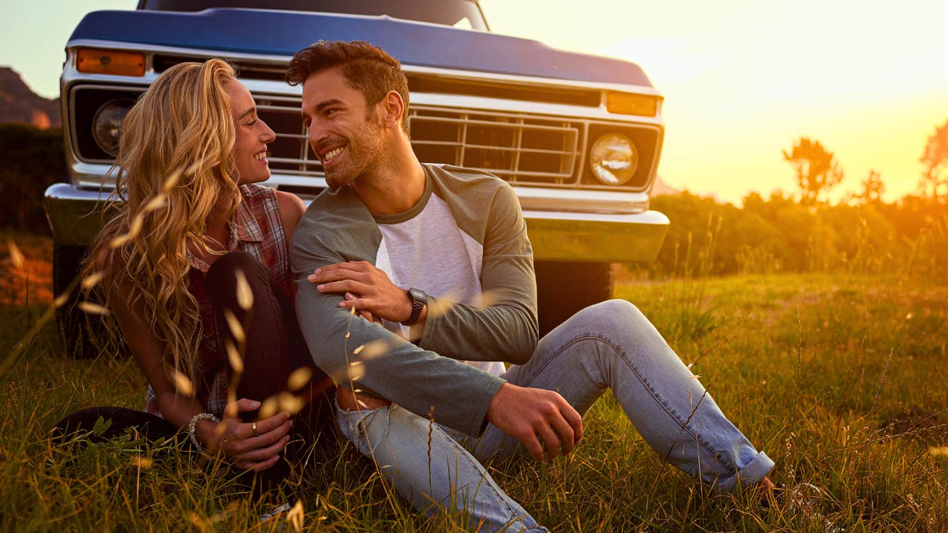 loving couple sitting in the grass in front of a car