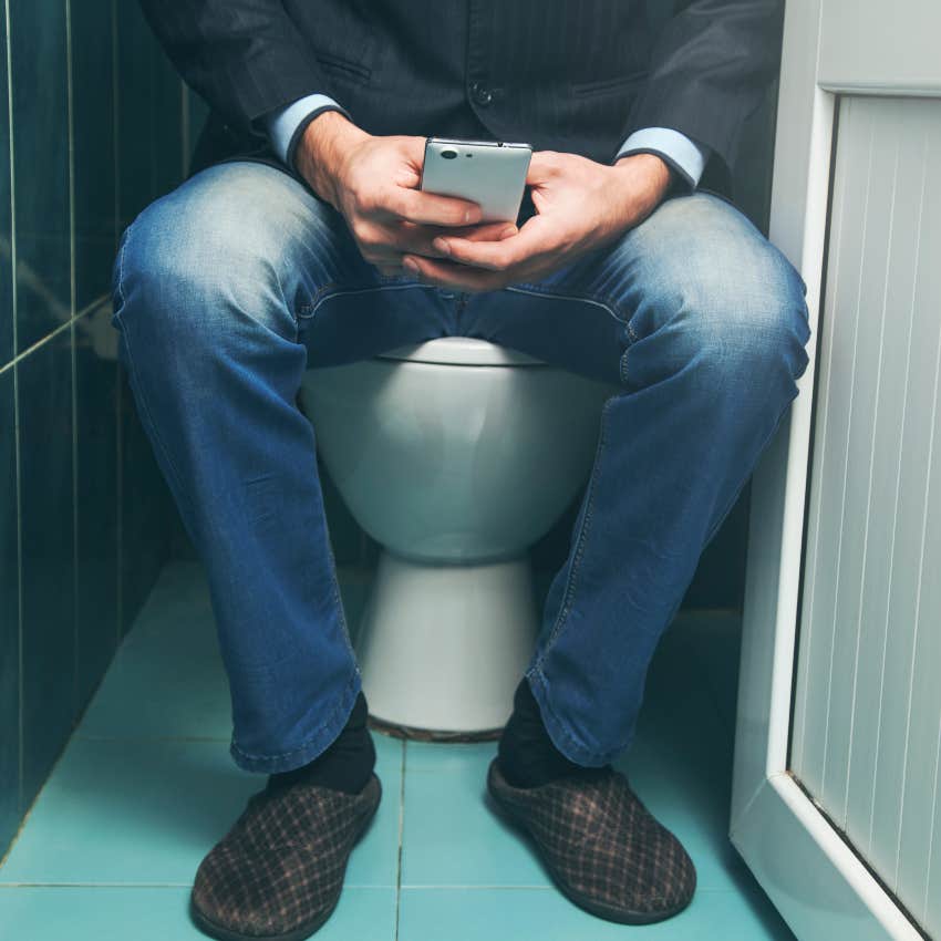 man sitting on toilet using phone