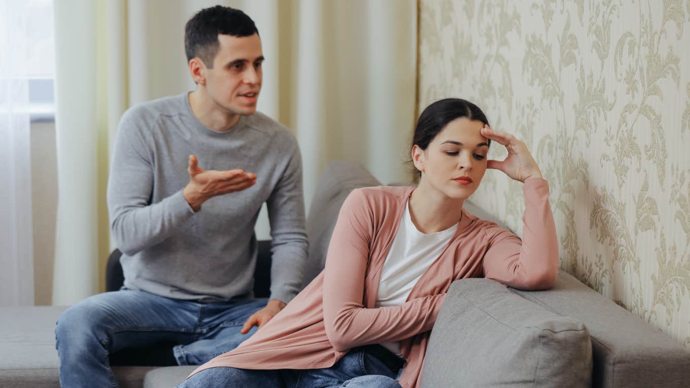 husband arguing with annoyed wife whose back is to him while sitting on couch