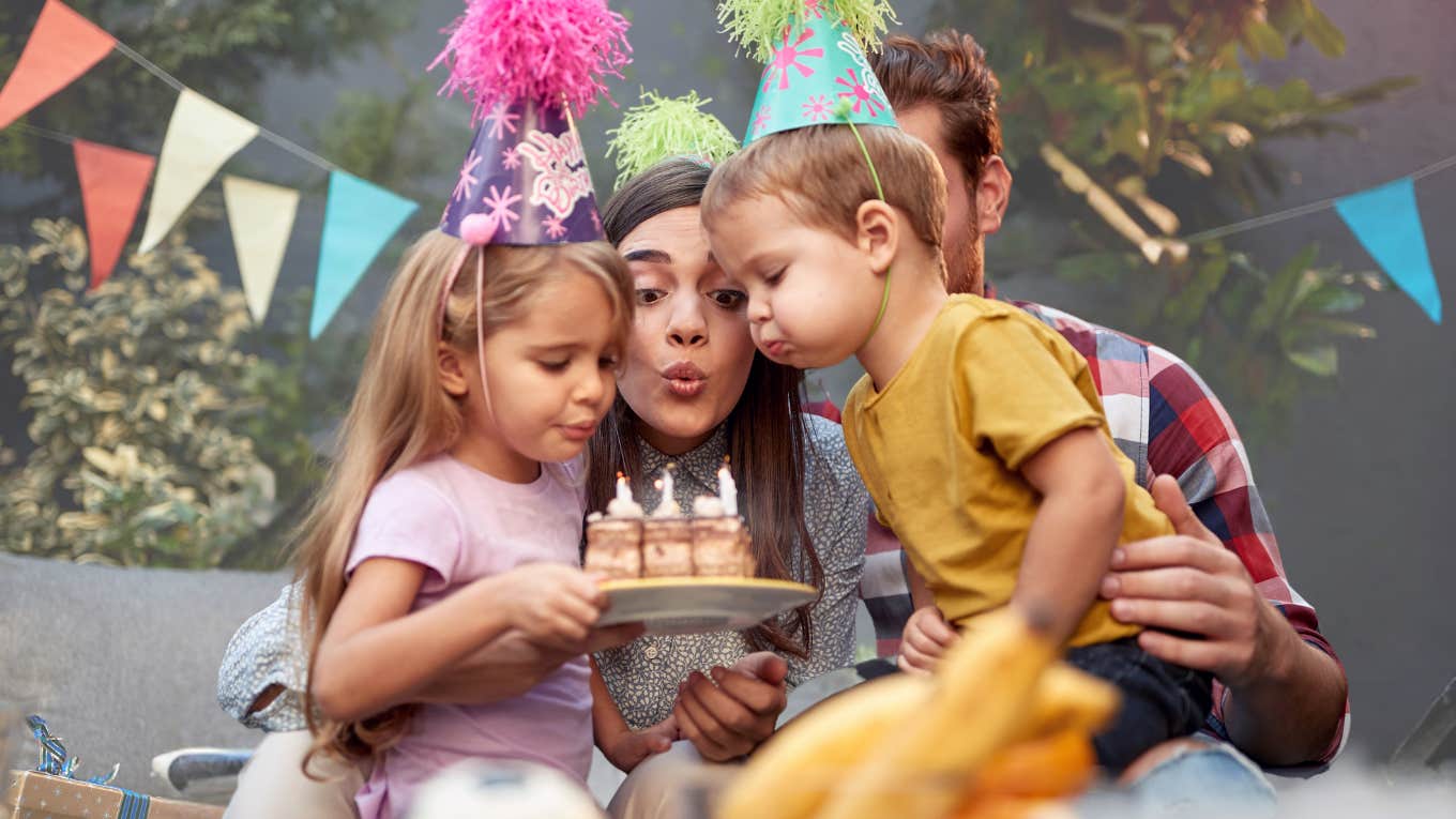 Mom letting siblings blow out birthday candles. 