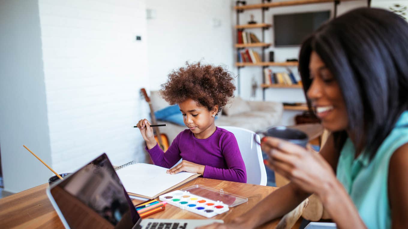 mom working on computer with daughter sitting next to her painting