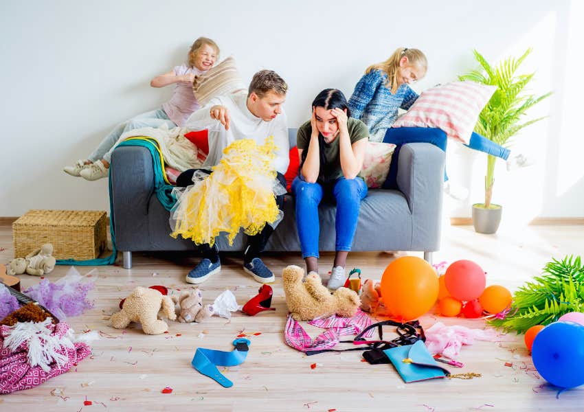 overwhelmed mom sitting on couch with husband and two kids looking at mess they made 