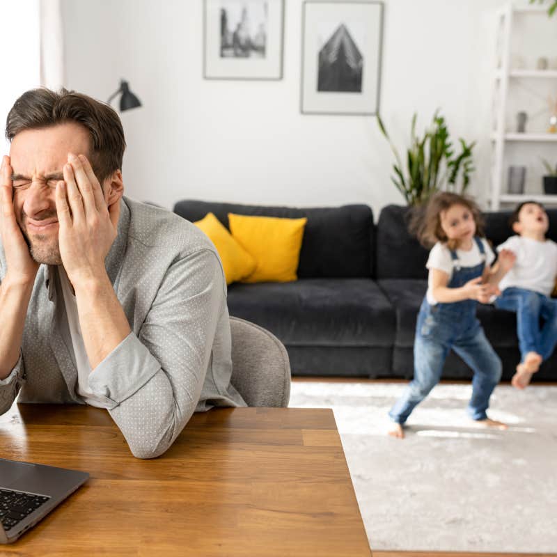 dad stressed while sitting in front of laptop with kids playing behind him