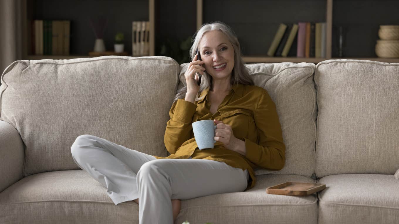 woman speaking on phone while sitting on couch and holding coffee mug