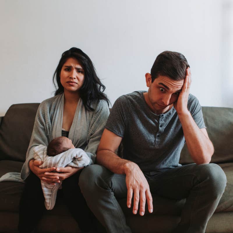 exhausted parents sitting on couch with newborn baby