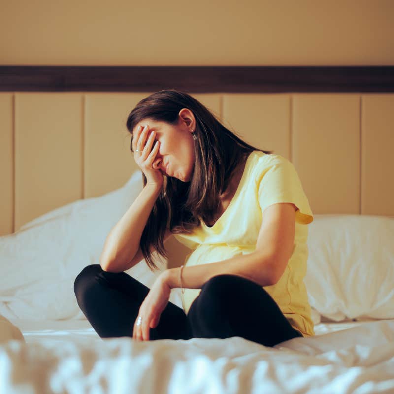 stressed woman sitting on bed with head in hand