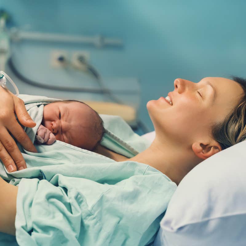 new mom lying down and cuddling newborn baby in hospital delivery room