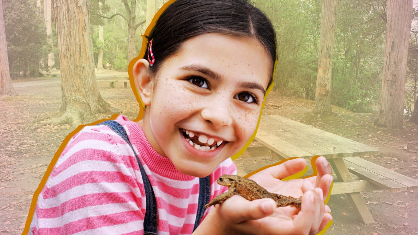 Young girl smiling holding a frog, reducing homesick anxiety at camp