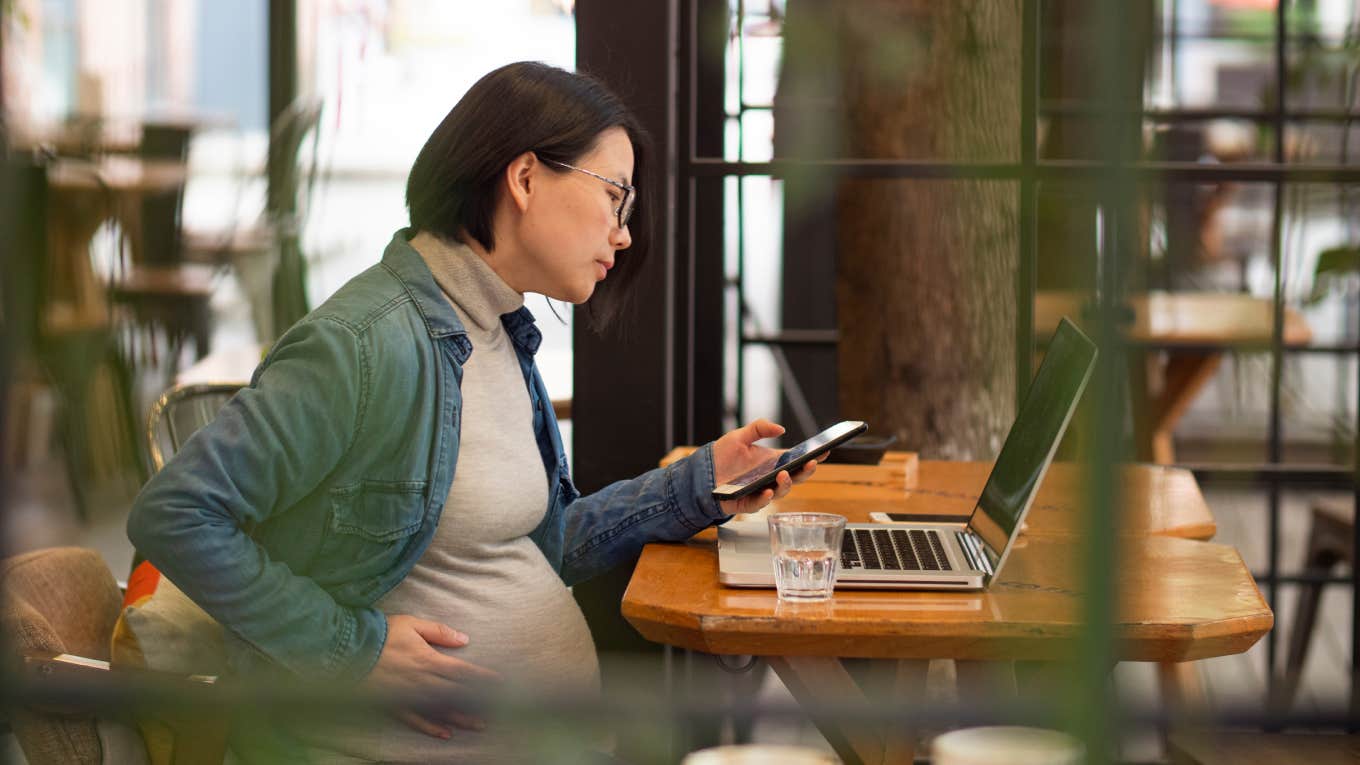 pregnant woman working with laptop using mobile phone in the cafe office