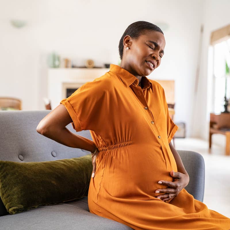 black expecting woman suffering from lower back pain sitting on sofa